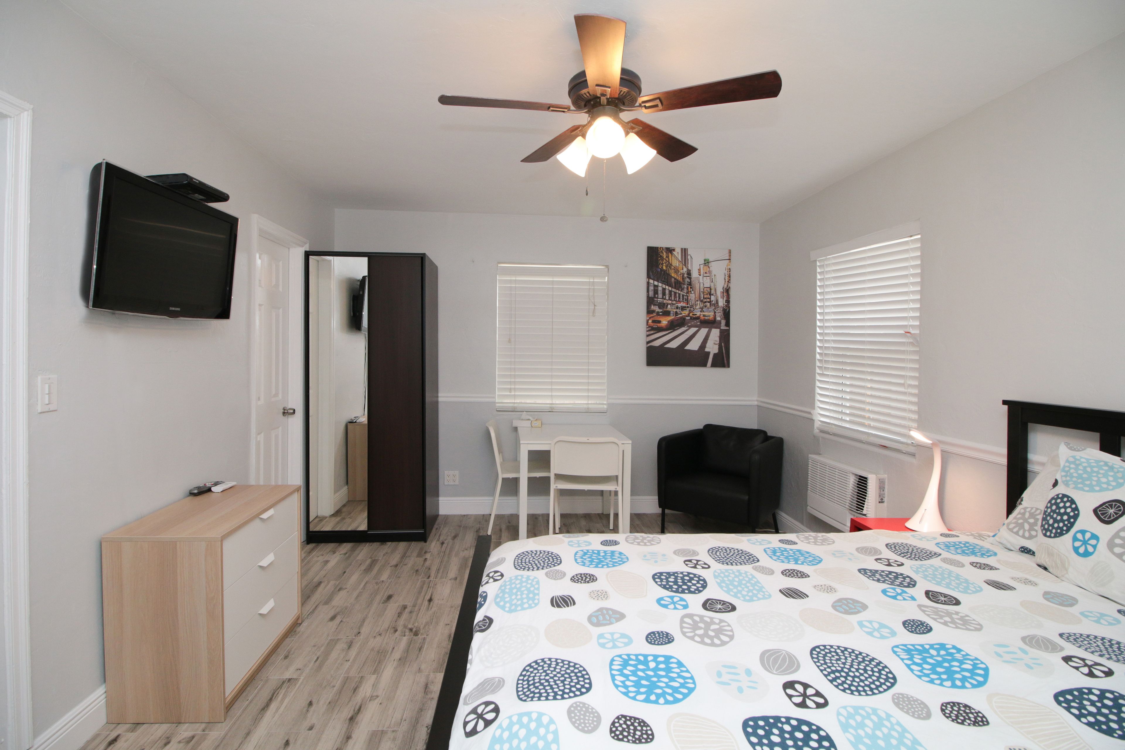A bedroom with a bed, a desk, a chair, a television, and a ceiling fan.