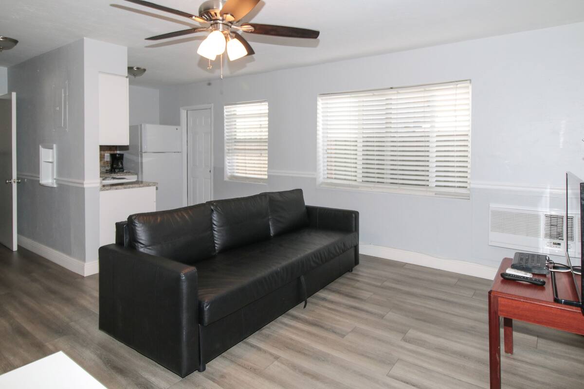 A living room with a black leather sofa, a ceiling fan, and a wooden coffee table.
