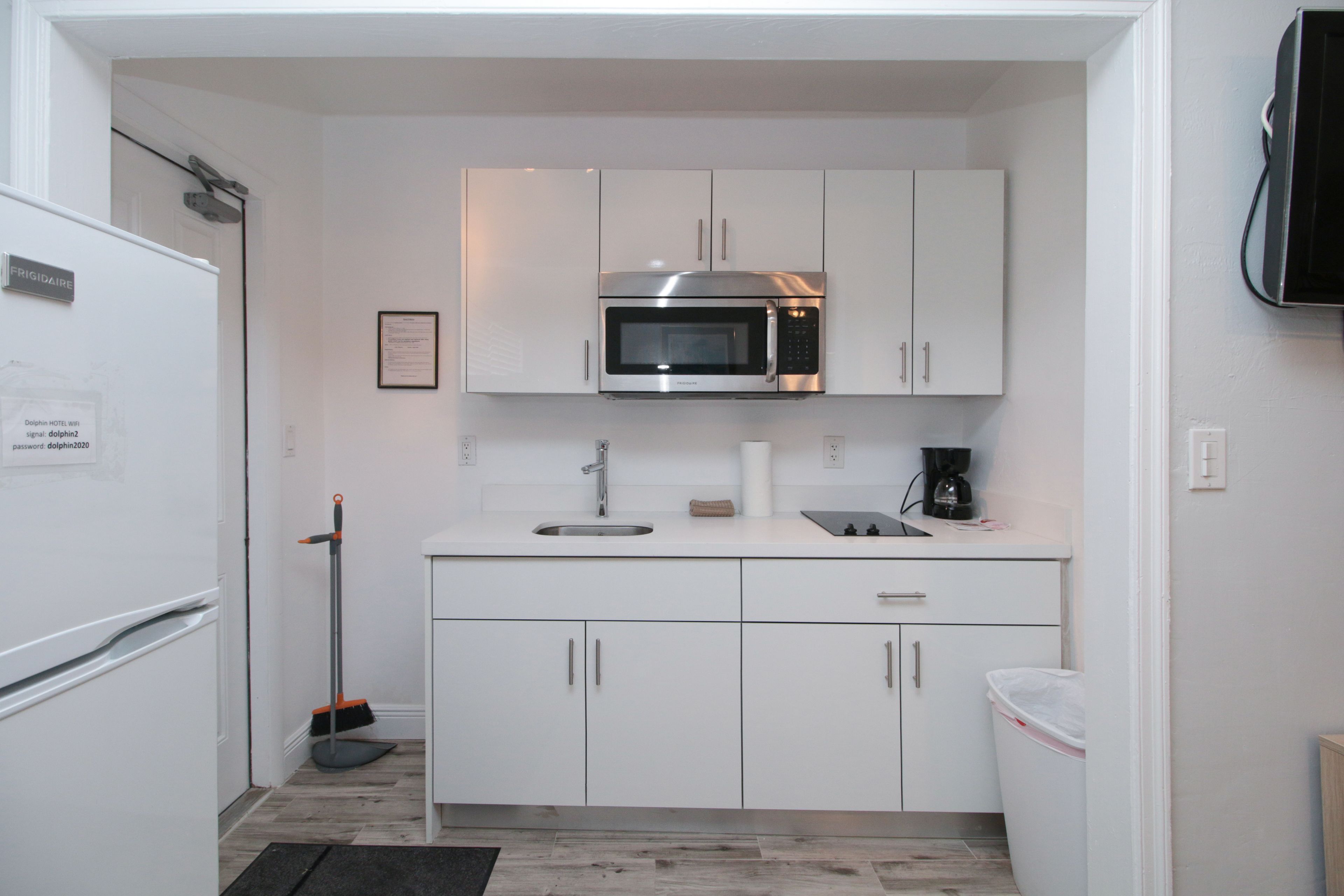 Cocina compacta con armarios blancos, un microondas de acero inoxidable, un lavamanos y una cafetera.