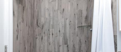 A shower with a wooden wall, a white curtain, and a tiled floor.