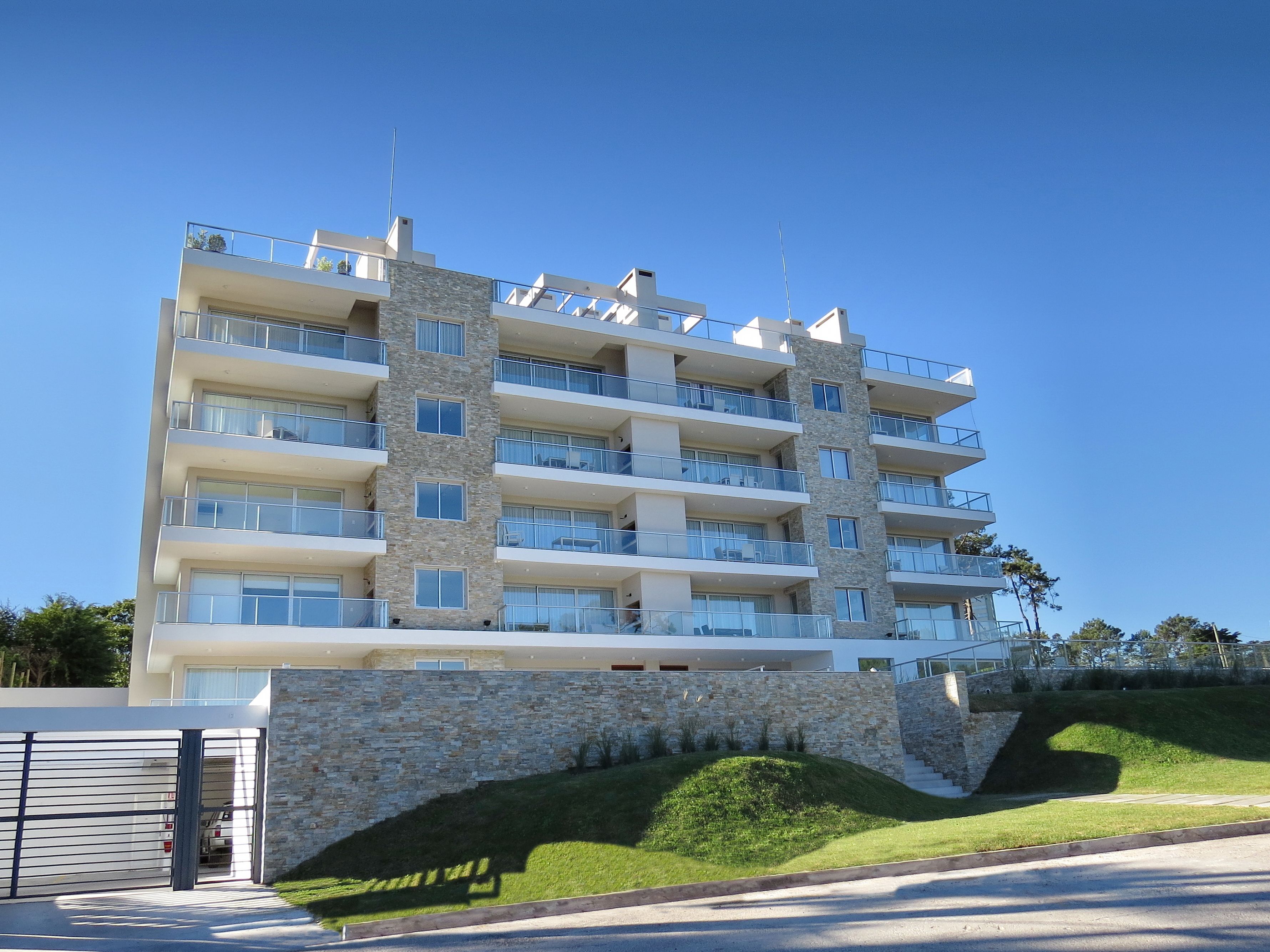 A multi-story hotel with balconies, a stone facade, and a parking area.