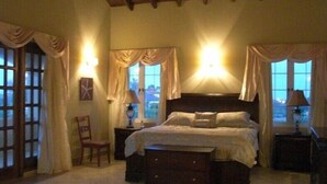Un dormitorio con una cama grande, dos mesitas de noche, una silla y una ventana con cortinas.