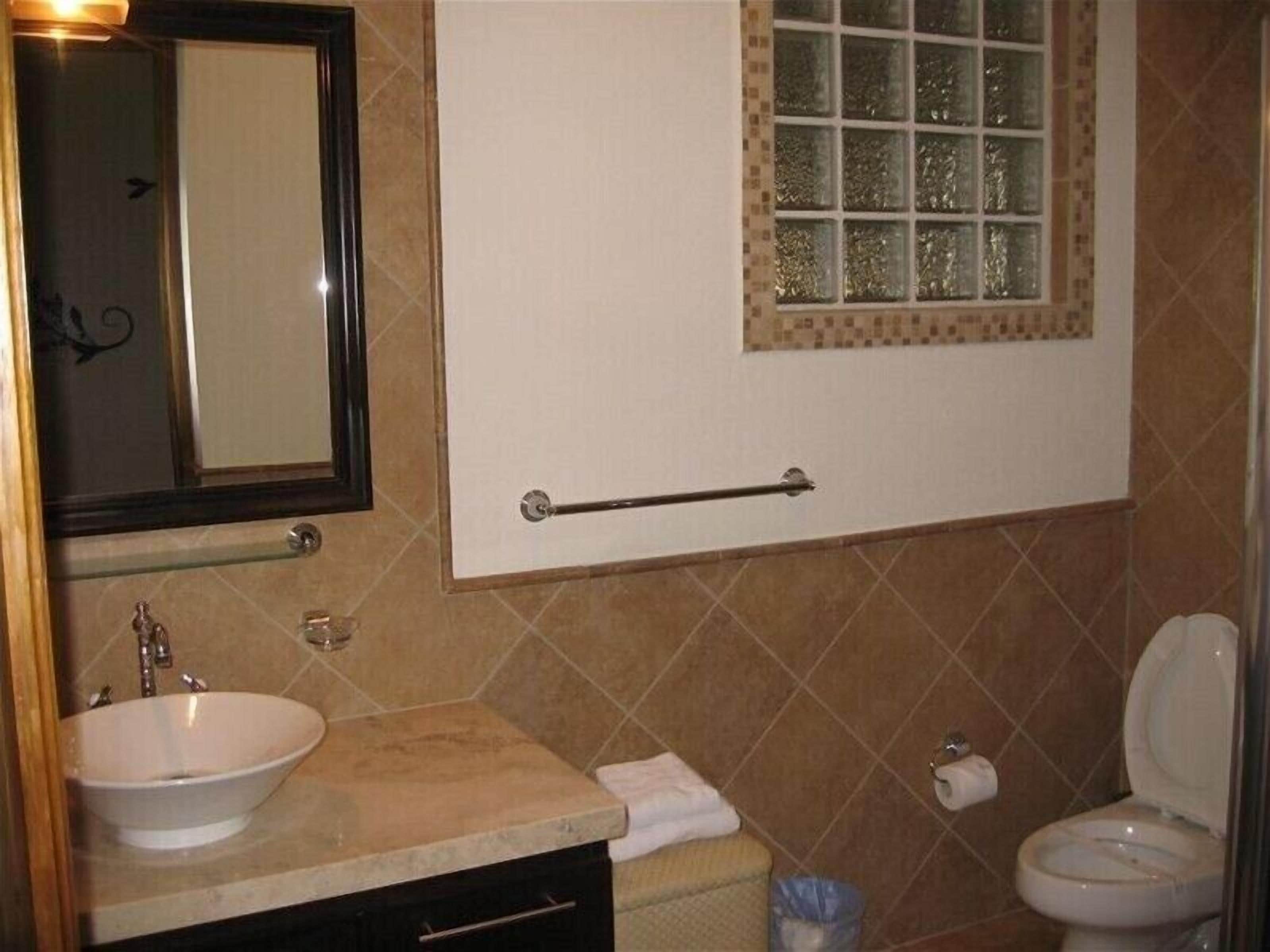 Une salle de bain équipée d’un lavabo, d’un miroir, d’un porte-serviettes, de toilettes et d’une fenêtre ornée d’un cadre décoratif.
