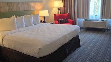 A hotel room with a large bed, a red armchair, a desk with a lamp, and a window with curtains.