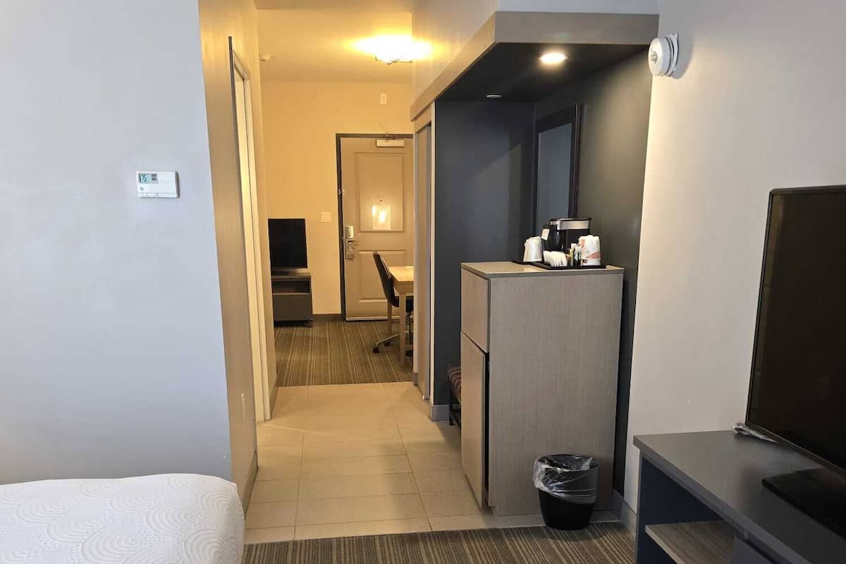 A hotel room with a bed, a desk, a television, a trash bin, and a hallway leading to a bathroom.