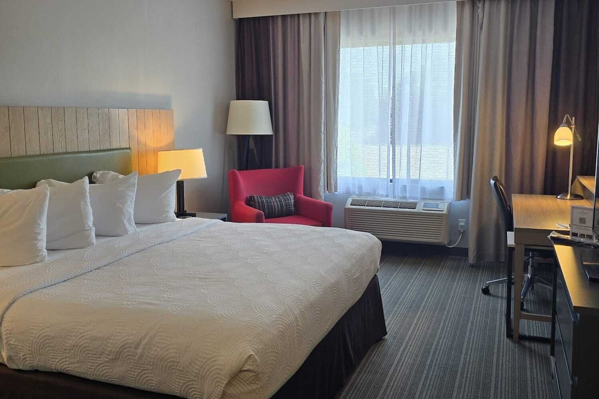 A hotel room with a large bed, a desk, a chair, a lamp, and a window with curtains.