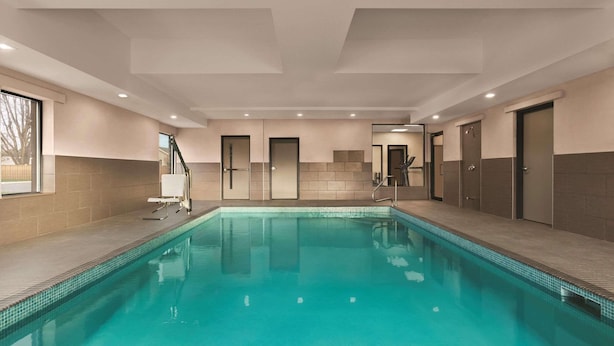 A swimming pool with a tiled edge, a ceiling with recessed lighting, and a door leading to a changing room. - Country Inn & Suites by Radisson, Belleville, ON (Belleville)
