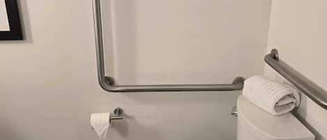 A white toilet with a handrail, a roll of toilet paper, and a towel on the tank.