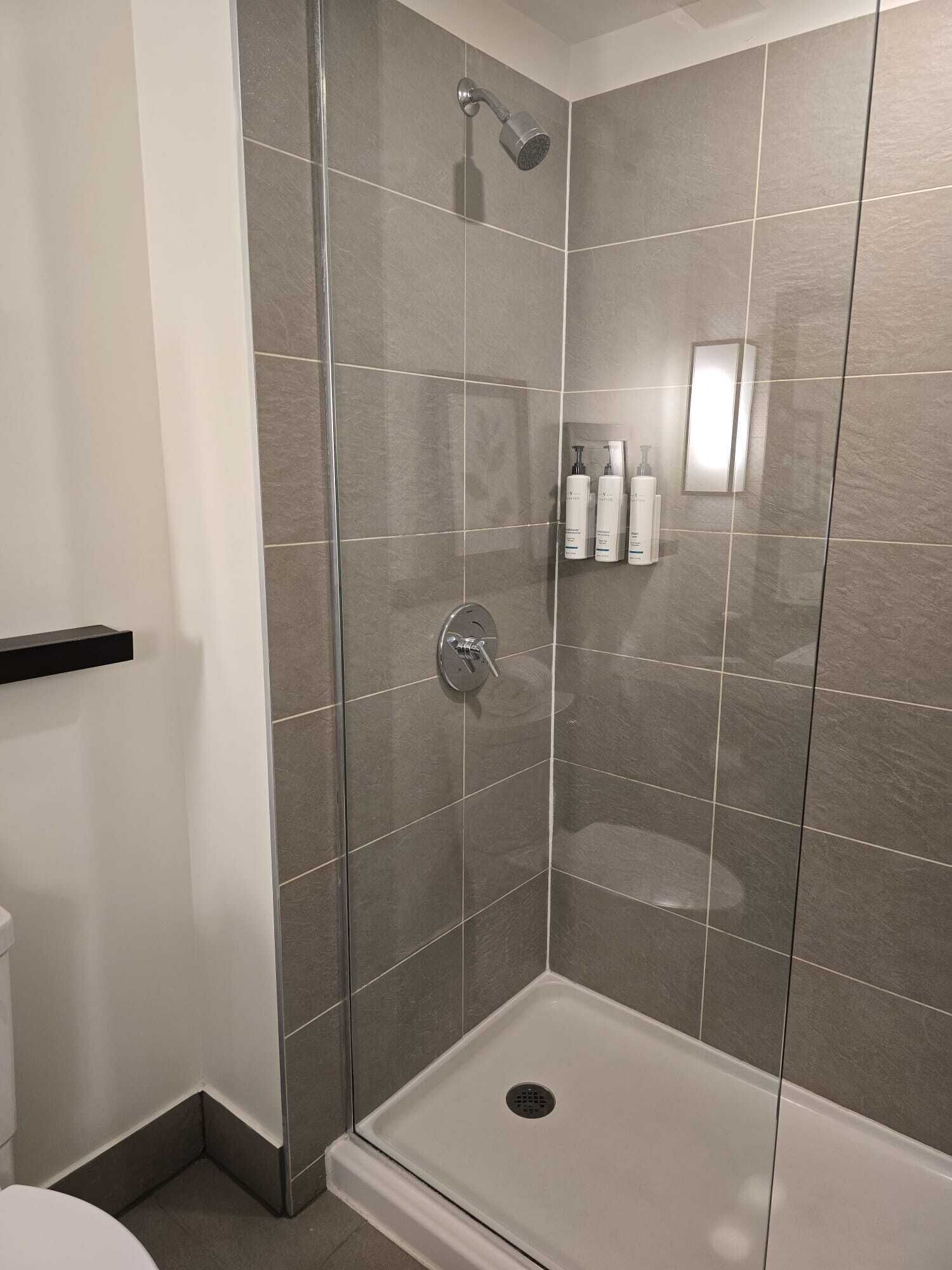 A shower area with a glass door, a handheld showerhead, and a wall-mounted light fixture.