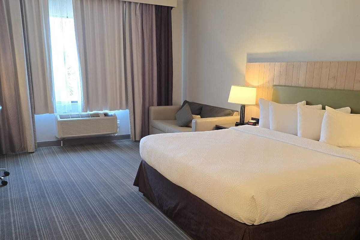 A hotel room with a large bed, a desk, a chair, and a window with curtains.