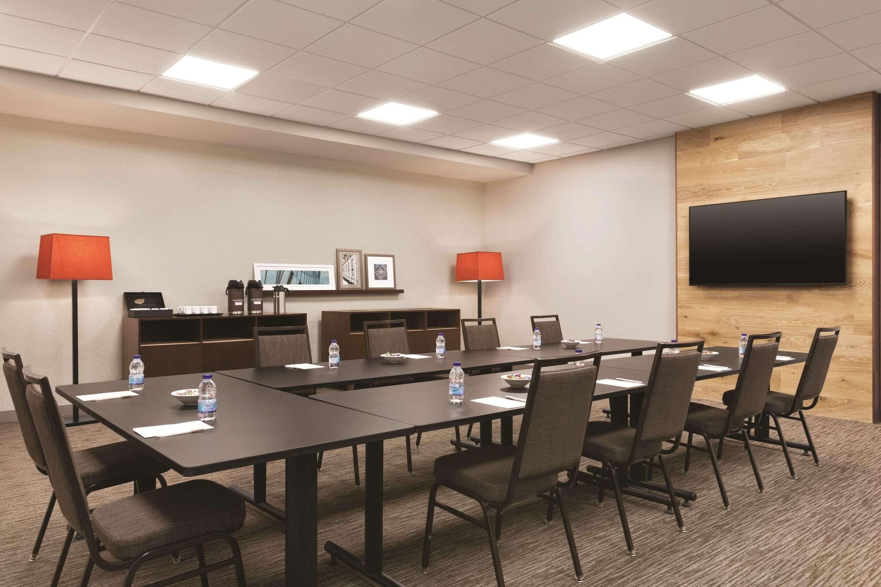 Une salle de conférence avec une longue table, des chaises, des bouteilles d’eau et un téléviseur à écran plat fixé au mur.