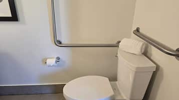 Uma sanita branca com barra de apoio, uma toalha no reservatório e um rolo de papel higiénico na parede.