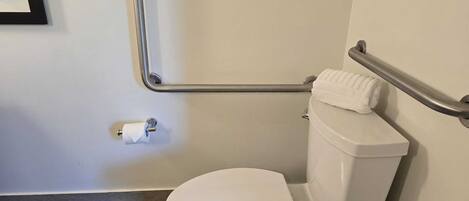 A white toilet with a grab bar, a towel on the tank, and a toilet paper holder on the wall.