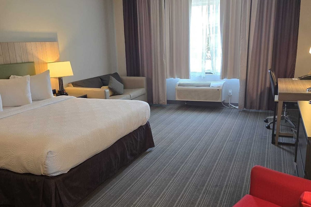 A hotel room with a large bed, a desk, a chair, and a window with curtains.