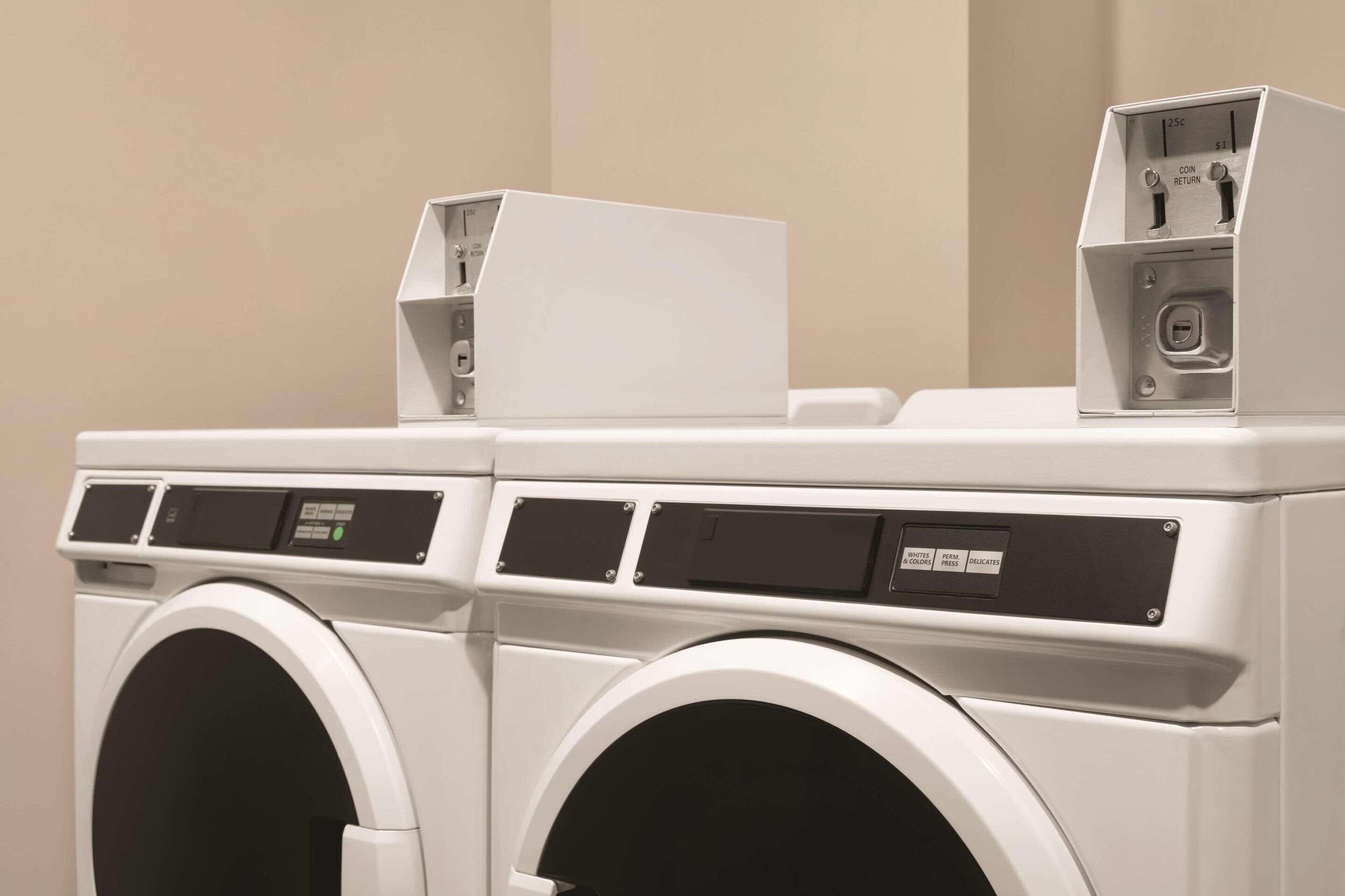 A front view of a modern, white, stacked washer and dryer unit with control panels and a coin return slot.