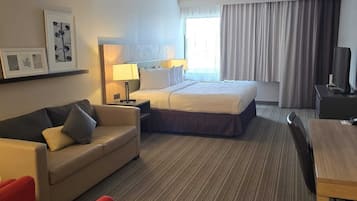 A hotel room with a bed, a desk, a chair, a sofa, and a TV.
