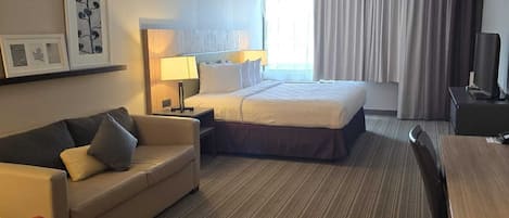 Une chambre d’hôtel équipée d’un lit, d’un bureau, d’une chaise, d’un canapé et d’une télévision.