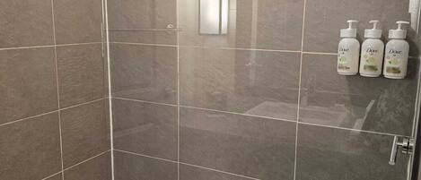Douchegedeelte met betegelde wanden, een glazen deur en drie Dove shampoo flessen aan de muur.