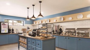 A kitchen with blue cabinets, a central island with drawers, overhead pendant lights, and a display of baked goods. - Country Inn & Suites by Radisson, Belleville, ON (Belleville)
