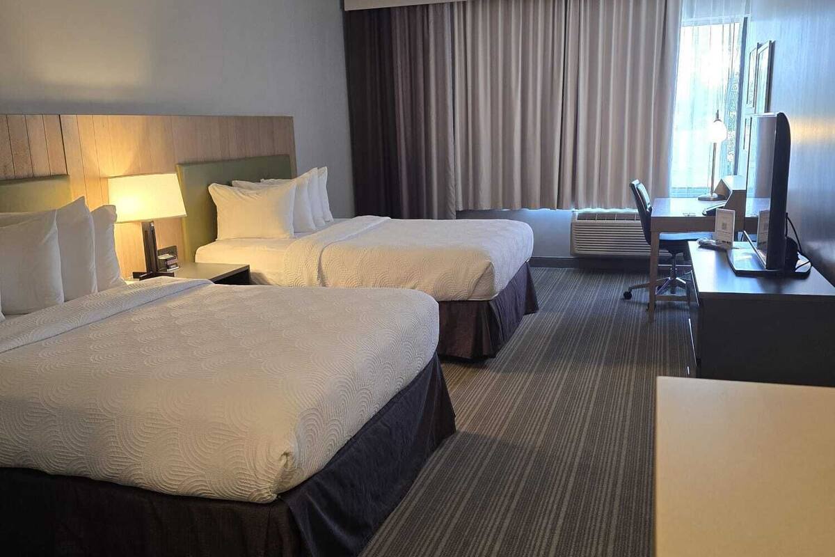 A hotel room with two beds, a desk, a chair, a TV, and a window with curtains.