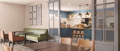 Un comedor con mesas y sillas, un sofá verde y una cocina al fondo.