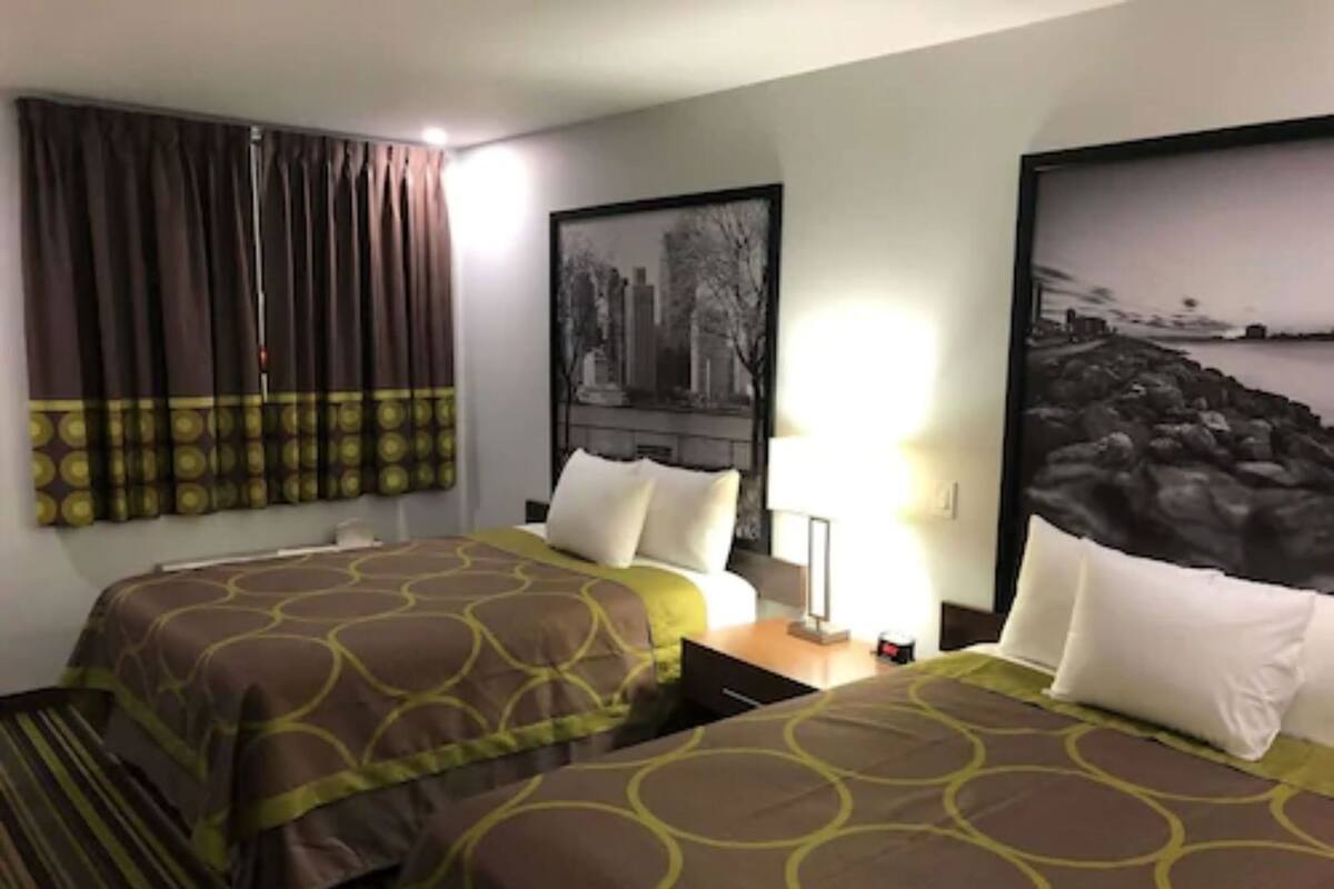 Una habitación de hotel con dos camas, una mesita de noche, una lámpara y dos cuadros en las paredes.