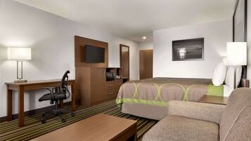 Habitación de hotel con cama, escritorio, silla, televisión, espejo y un cuadro en la pared.