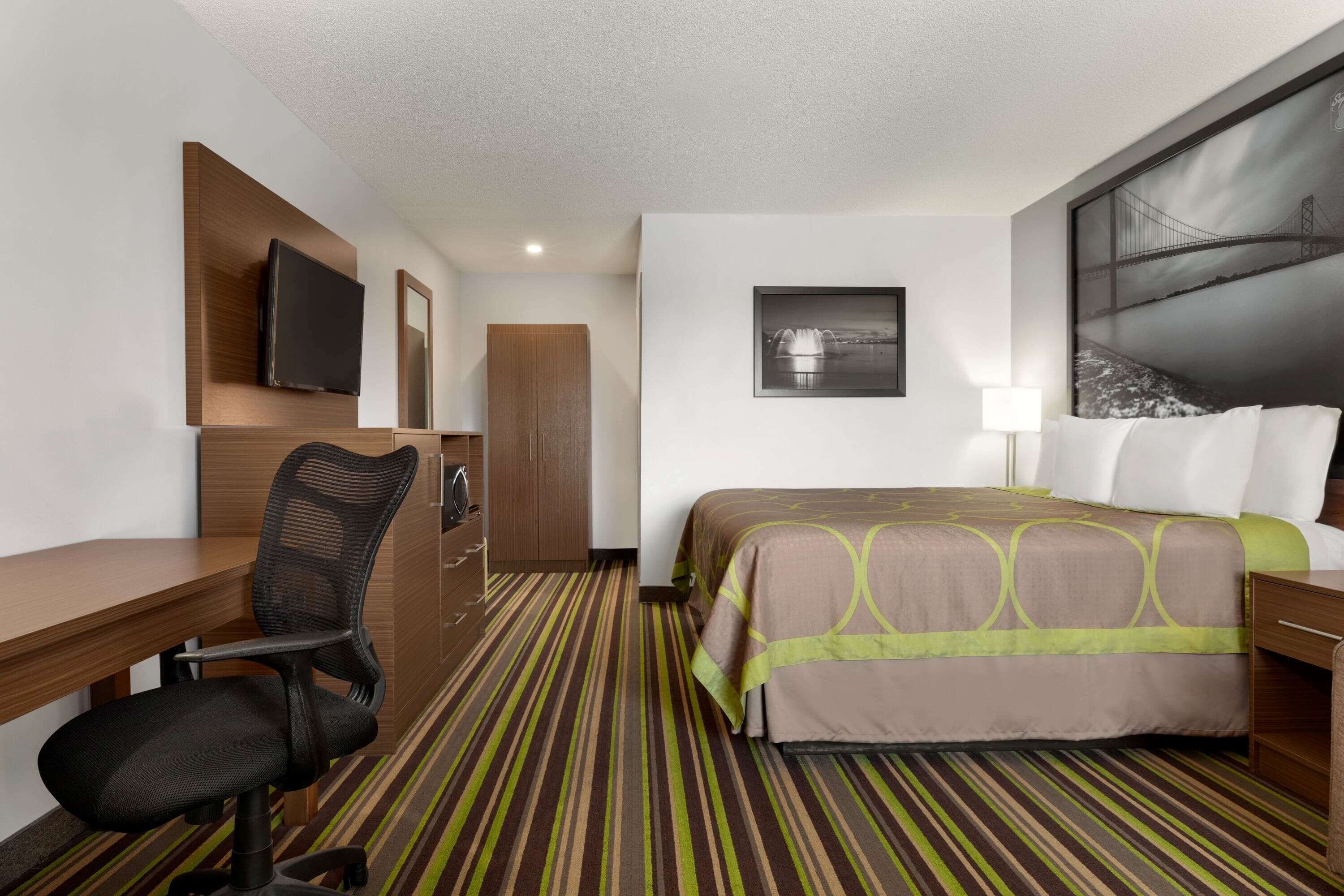 A hotel room with a bed, desk, chair, TV, and artwork on the walls.
