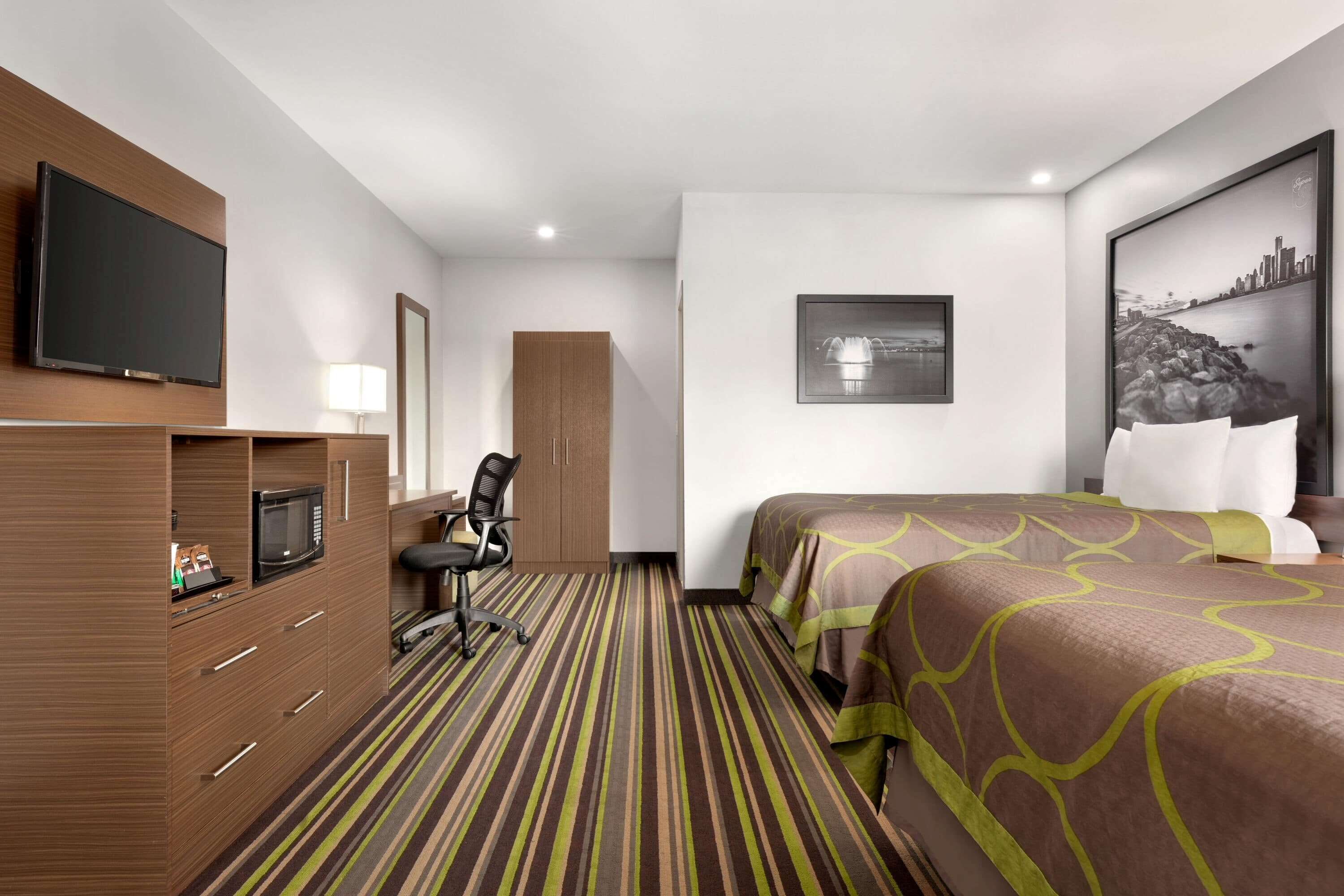 Una habitación de hotel con cama, escritorio, silla, televisor y una ventana grande.