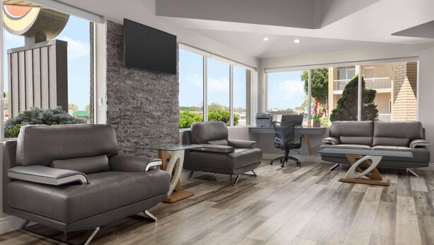 A modern living room with grey sofas, a stone accent wall, and large windows offering a view of the outdoors.