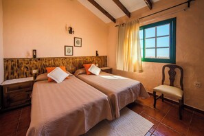 A bedroom with two beds, a wooden headboard, a chair, and a window with curtains. - Casas Rurales Herreñas (Valverde)