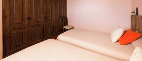 A bedroom with two beds, wooden wardrobes, and a small bedside table.