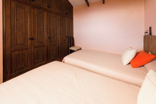 A bedroom with two beds, wooden wardrobes, and a small bedside table.