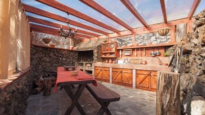 A rustic outdoor kitchen with a stone wall, wooden beams, and a wooden table with a bench. - Casas Rurales Herreñas (Valverde)