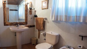 A bathroom with a sink, toilet, bidet, and a mirror with a wooden frame.