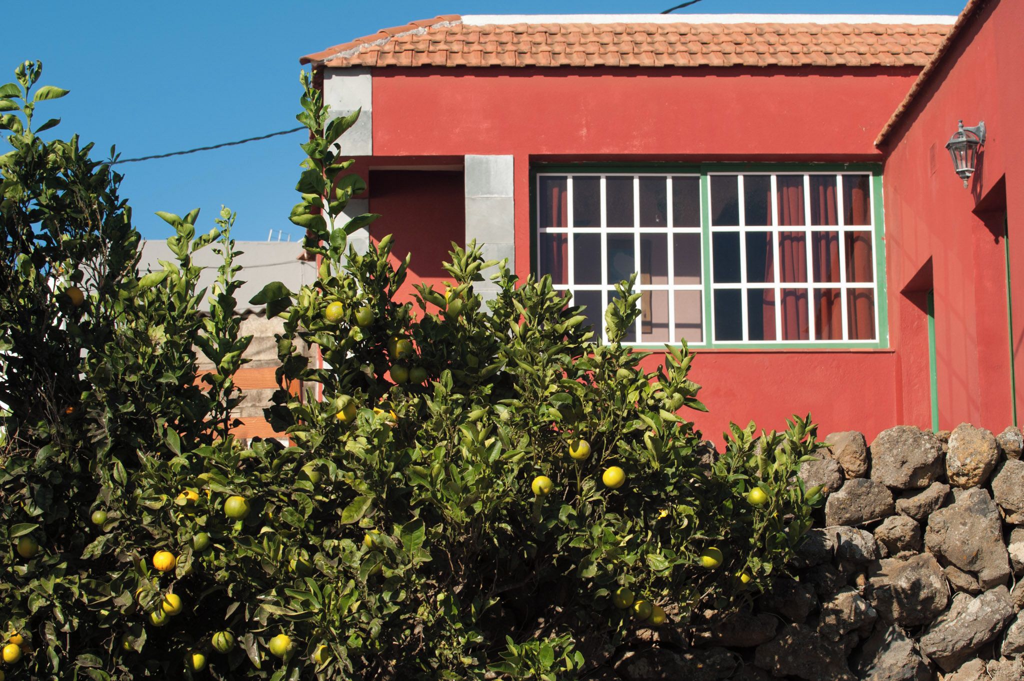 Un edificio rojo con una ventana y un muro de piedra al frente.