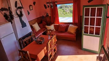 Una habitación acogedora con un sofá de madera, una mesa de comedor con sillas, un refrigerador y una ventana con cortinas.