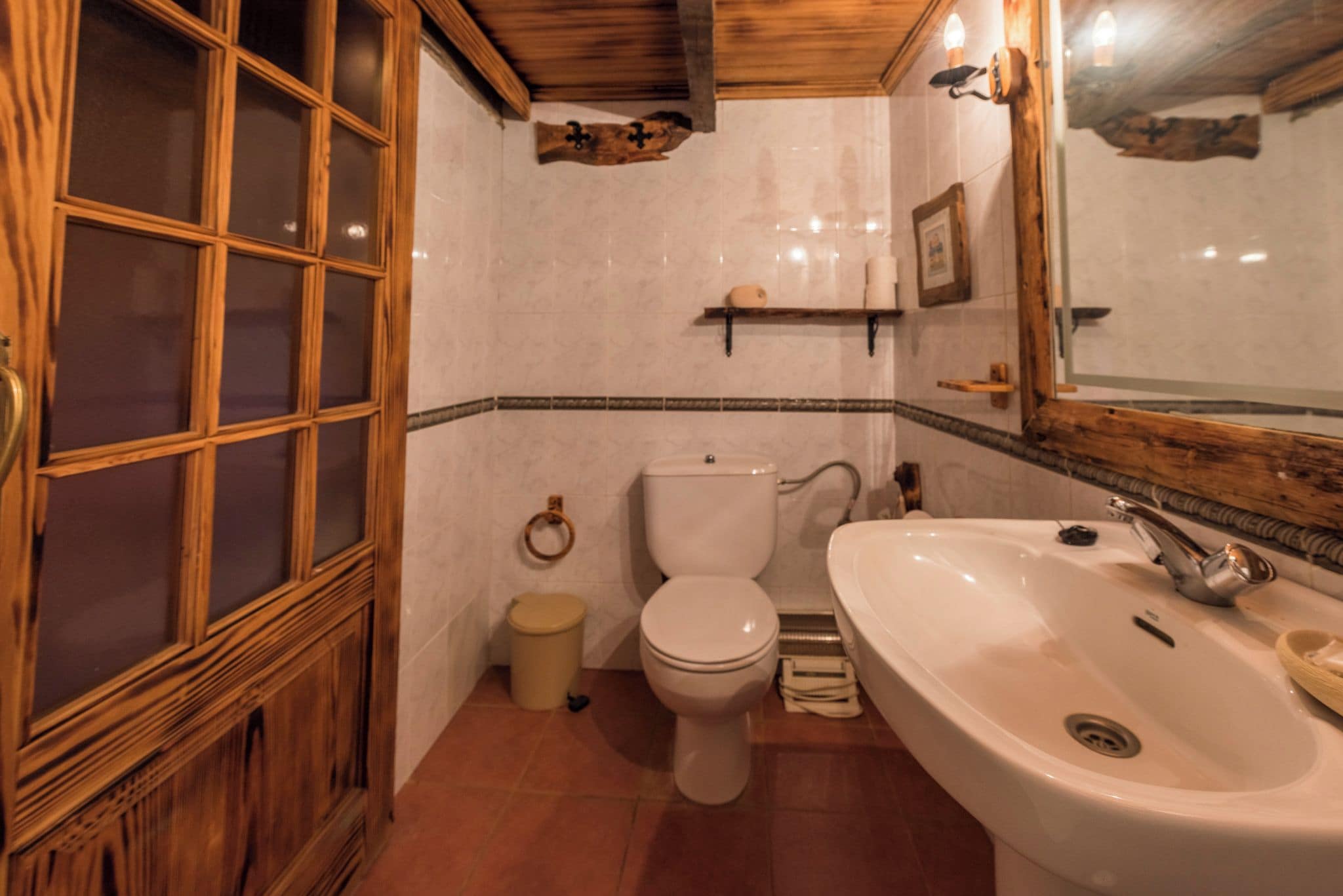 A bathroom with a wooden door, a toilet, a sink, and a mirror.