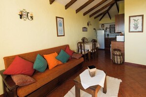 A cozy living area with a sofa, a dining table, and chairs. There is a kitchen in the background with a refrigerator and a sink. - Casas Rurales Herreñas (Valverde)