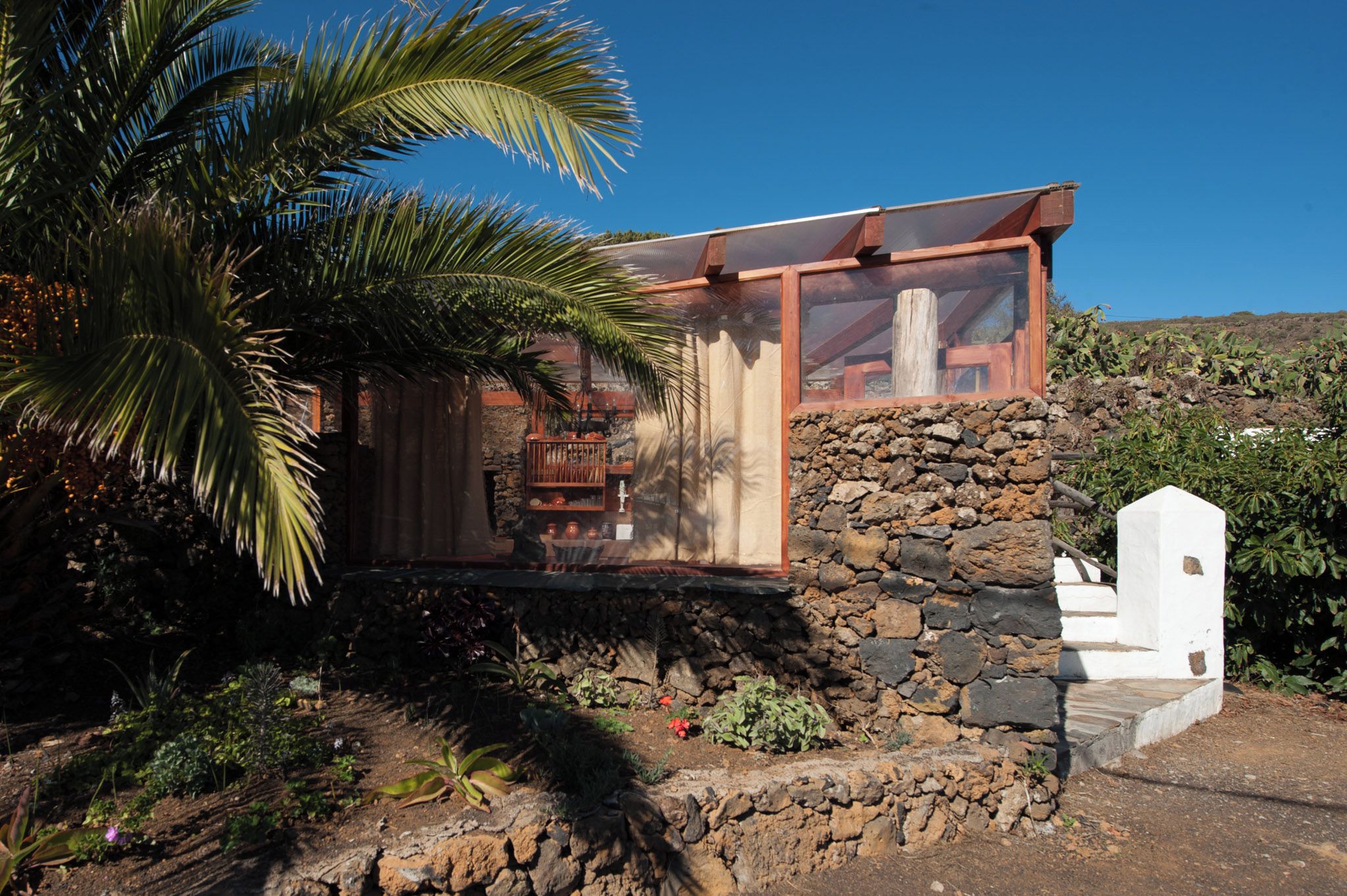 Una casa moderna amb fonamentació de pedra, façana de vidre i una palmera al primer pla.