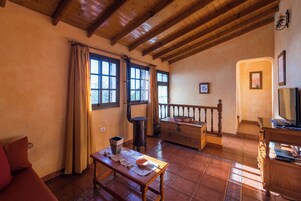 Una sala de estar acogedora con techo de madera, un sofá, una mesa con un cuenco y una escalera que conduce a otra habitación.