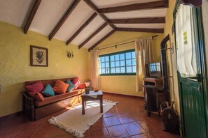 A cozy living room with a wooden sofa, a television, and a green door. - Casas Rurales Herreñas (Valverde)