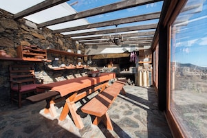 Un área de comedor al aire libre rústica, con bancos de madera y paredes de piedra.