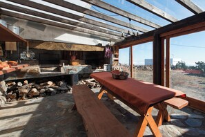 A rustic outdoor kitchen with a stone hearth, wooden benches, and a view through large windows. - Casas Rurales Herreñas (Valverde)