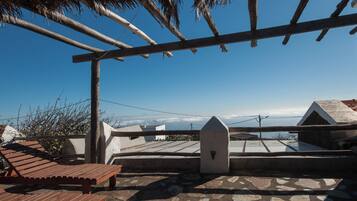 Una terrazza sul tetto con una pergola in legno, pavimento in pietra e vista sul cielo e sulle nuvole.
