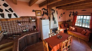 A rustic kitchen with a tiled backsplash, wooden cabinets, a gas stove, and a dining area with a table and chairs. - Casas Rurales Herreñas (Valverde)