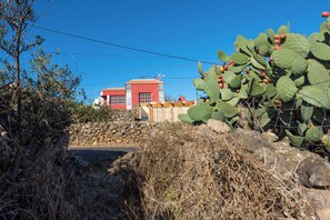 A red building with a stone wall and cactus plants in the foreground.
