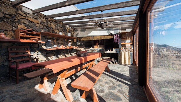 A rustic outdoor dining area with wooden benches and a stone wall backdrop.