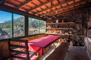 L’intérieur d’un chalet rustique, avec une table en bois, des bancs, des étagères remplies d’ustensiles de cuisine et un mur en pierre.