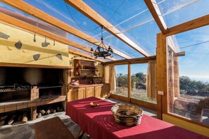 A rustic kitchen with a brick oven, wooden cabinets, and a dining table set for two. - Casas Rurales Herreñas (Valverde)